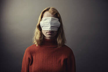 Teenage girl wearing protective face mask on eyes while standing against gray background - JATF01286