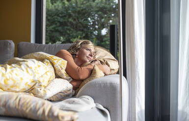 Thoughtful woman looking through window while lying on sofa at home - BFRF02309