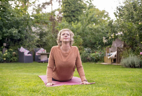 Woman doing yoga while lying on exercise mat at back yard - BFRF02317