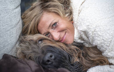 Smiling woman embracing Briard on sofa - BFRF02324