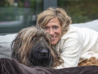 Smiling woman embracing dog while sitting on sofa at back yard - BFRF02325