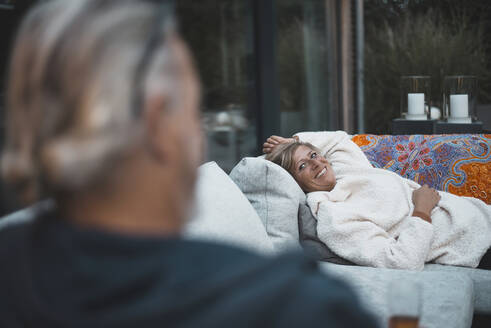 Lächelnde Frau, die einen Mann ansieht, während sie sich auf dem Sofa im Hinterhof entspannt - BFRF02326