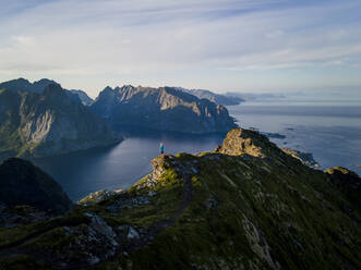 Frau bewundert die Aussicht auf die Berge, während sie auf einem Berg in Reine, Lofoten, Norwegen, steht - MALF00171