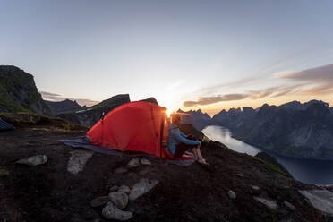 Frau im Lager auf einem Berg während des Sonnenuntergangs auf Reinebringen, Lofoten, Norwegen - MALF00189