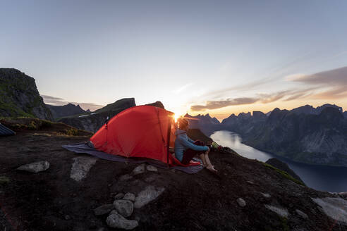 Frau im Lager auf einem Berg während des Sonnenuntergangs auf Reinebringen, Lofoten, Norwegen - MALF00189