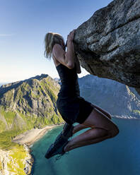 Frau, die an der Bergkante gegen den klaren Himmel in Ryten, Lofoten, Norwegen, hängt - MALF00212