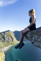 Forscher, der die Aussicht betrachtet, während er auf einem Berg in Ryten, Lofoten, Norwegen, sitzt - MALF00216