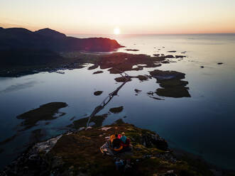 Erwachsener Mann und Frau bewundern die Aussicht, während sie auf einem Berg bei Volandstinden, Lofoten, Norwegen, sitzen - MALF00237