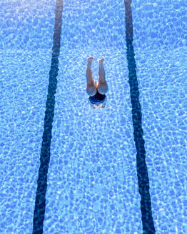 Junge Frau, die an einem sonnigen Tag ins Schwimmbad springt - STSF02676