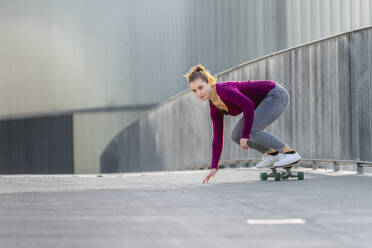 Junge Frau, die auf einer Fußgängerbrücke Skateboard fährt - STSF02678