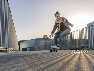 Young woman skateboarding on footbridge in city against clear sky - STSF02680