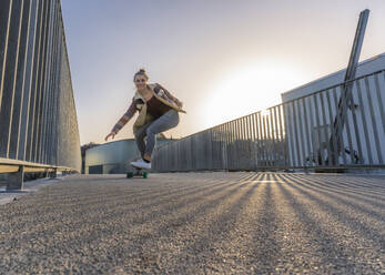 Glückliche Frau auf dem Skateboard gegen den klaren Himmel bei Sonnenuntergang - STSF02682