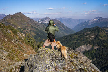 Männlicher Wanderer und Hund genießen die Aussicht vom Gipfel - CAVF91087