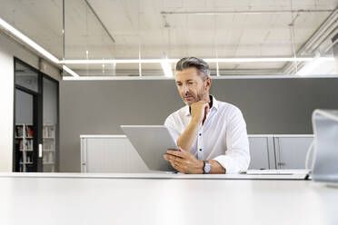 Geschäftsmann, der ein digitales Tablet benutzt, während er im Büro sitzt - PESF02250