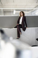 Selbstbewusste Geschäftsfrau, die mit übereinander geschlagenen Beinen auf einem Tablet im Büro sitzt - PESF02258