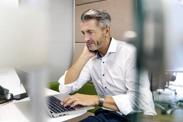 Geschäftsmann, der einen Laptop benutzt, während er am Schreibtisch im Büro sitzt - PESF02272