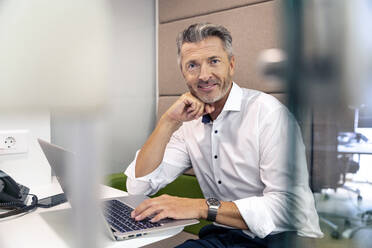 Lächelnder Geschäftsmann bei der Arbeit am Laptop im Büro - PESF02273