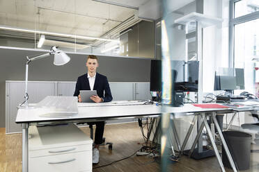 Young businessman wearing suit using digital tablet while sitting at office - PESF02279