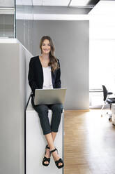 Junge Geschäftsfrau lächelt bei der Arbeit am Laptop im Büro - PESF02290