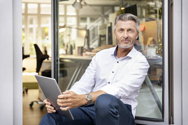 Älterer Geschäftsmann mit digitalem Tablet an der Bürotür sitzend - PESF02308