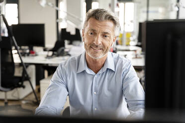 Smiling businessman sitting at office - PESF02344