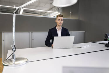 Junger Geschäftsmann mit Laptop im Büro sitzend - PESF02361