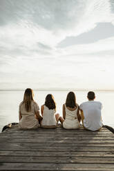 Parents with children looking at lake while sitting at jetty against sky - RCPF00321