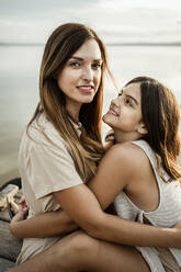 Mother and daughter embracing each other at jetty against lake - RCPF00342