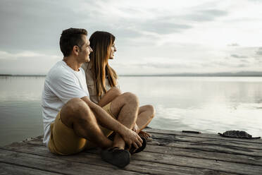 Relaxed mature couple looking away while sitting on jetty against sky - RCPF00350