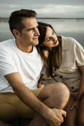 Mature woman leaning on man's shoulder while sitting at jetty - RCPF00351