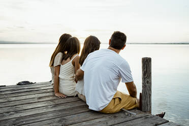 Familie bewundert den See, während sie am Steg sitzt - RCPF00358