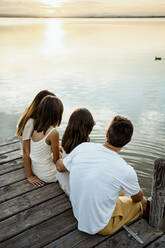 Familie bewundert den See, während sie bei Sonnenuntergang am Steg sitzt - RCPF00359