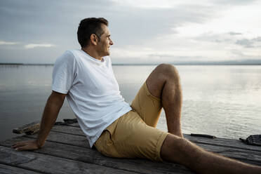 Älterer Mann verbringt seine Freizeit am Steg am See gegen den Himmel sitzend - RCPF00368