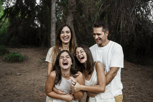 Eltern mit Töchtern, die lachend im Wald stehen, während sie im Urlaub sind - RCPF00400