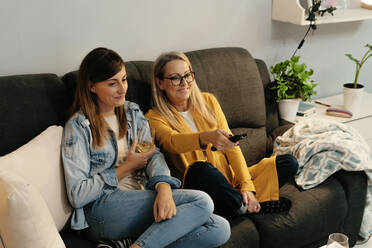 Lächelnde Mutter und Tochter sehen fern, während sie zu Hause auf dem Sofa sitzen - ERRF04705