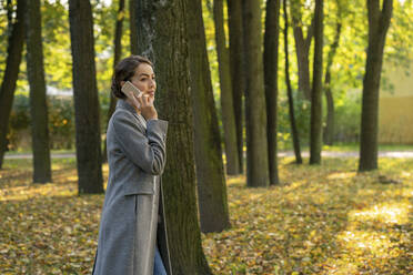 Weibliche Unternehmerin, die mit ihrem Smartphone telefoniert, während sie im Herbst im Park spazieren geht - VPIF03235