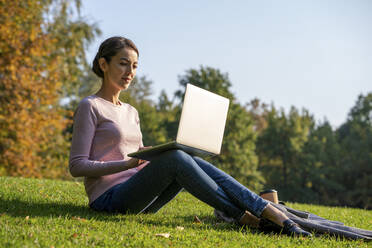 Young businesswoman using laptop while sitting in park during autumn - VPIF03250