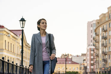 Weibliche Unternehmerin schaut weg, während sie im Herbst in der Stadt spazieren geht - VPIF03258