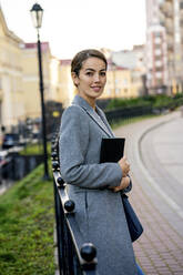 Unternehmerin hält Tagebuch und lehnt sich an ein Geländer in der Stadt im Herbst - VPIF03263