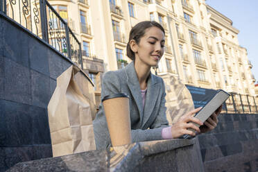 Unternehmerin, die ein digitales Tablet benutzt, während sie sich auf ein Geländer in der Stadt im Herbst stützt - VPIF03267