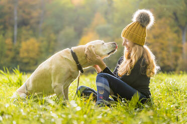 Happy woman playing with canine while sitting in park during autumn season - STSF02691