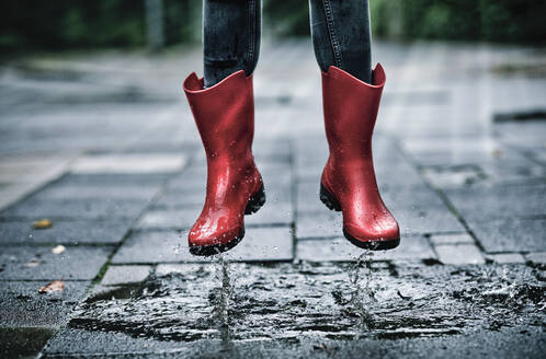 Feet of little girl wearing rubber boots jumping over small puddle - FLLF00518