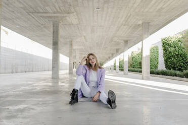 Young woman with head in hand sitting at parking lot - TCEF01382