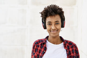 Smiling young Afro woman listening music against white wall - VEGF03171