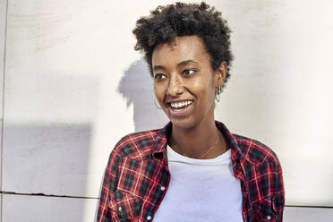 Lächelnde junge Afro-Frau, die gegen eine weiße Wand schaut - VEGF03188