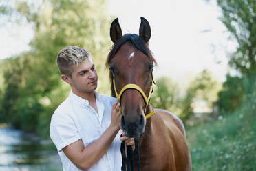 Porträt eines blonden jungen Mannes mit einem Pferd - CAVF91142