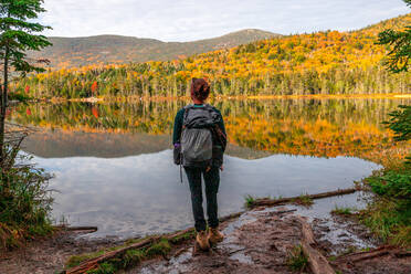 Young woman staring out at colorful trees reflecting in lake water. - CAVF91143