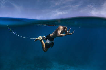 Surfer ohne Hemd mit Surfbrett-Leine schwimmt unter Wasser auf den Malediven - KNTF05958