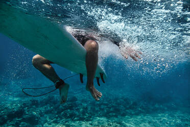 Männlicher Surfer auf dem Surfbrett sitzend beim Surfen im Meer auf den Malediven - KNTF05984