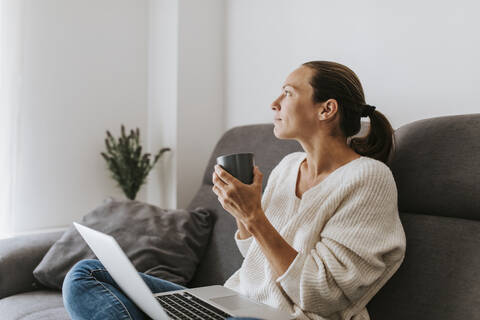 Thoughtful woman holding cup while looking away at home stock photo